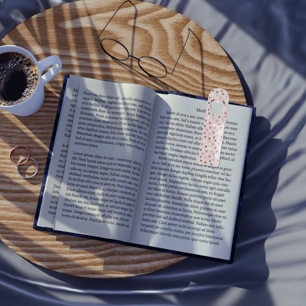 Colorful hearts aluminum bookmark holding page in open book on wooden surface with glasses and coffee cup nearby