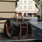 Black Blessed travel bag with brown PU leather handles, adjustable shoulder strap, gold zipper, and durable nylon material for versatile use