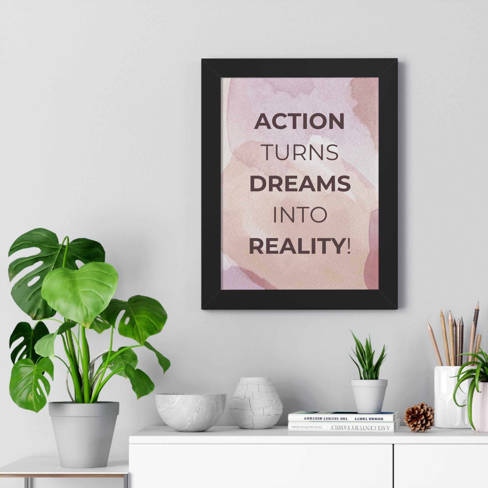 Motivational Dream to Reality poster with inspirational quote in modern black frame on wall above desk with plants and decor