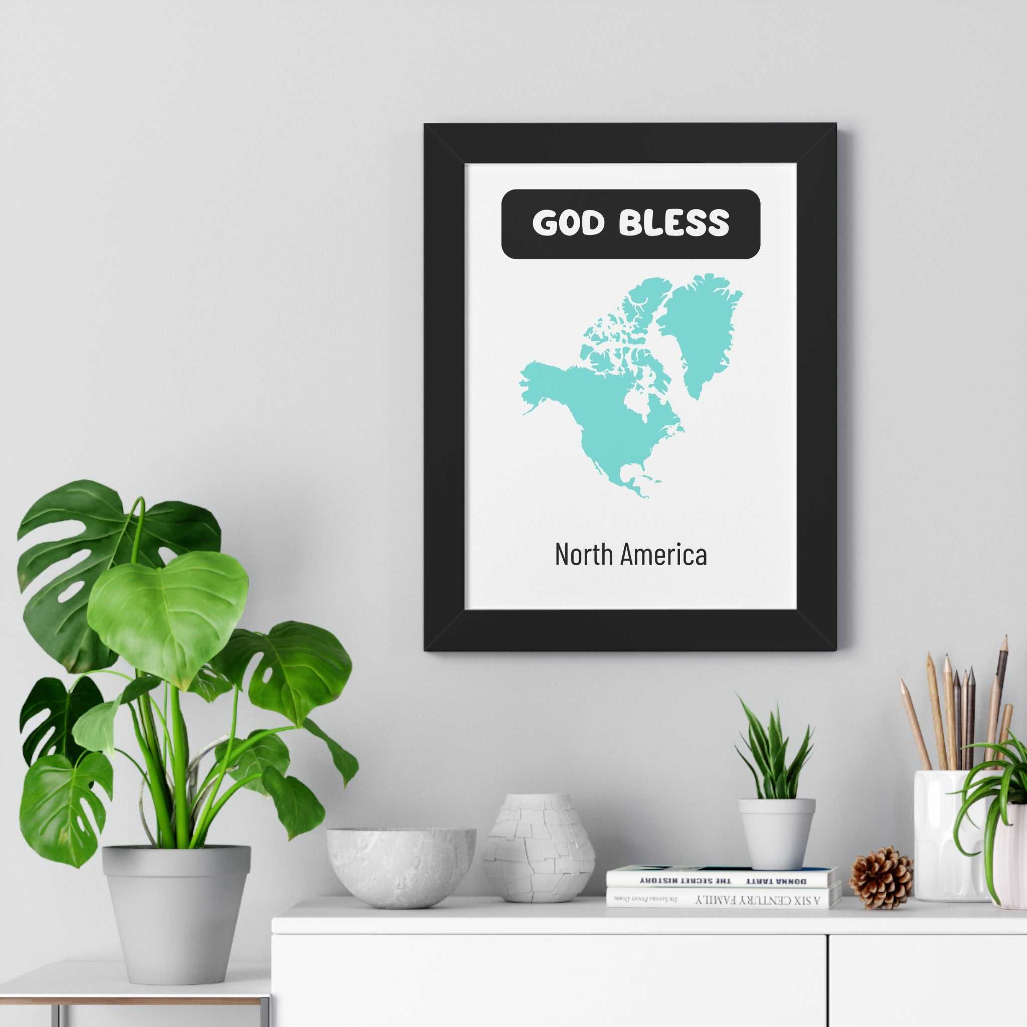 God Bless North America poster with map design in black frame on wall above white shelf with plants and decor