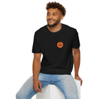 Man wearing black Divine Perfection t-shirt with orange emblem and light blue jeans sitting on white block