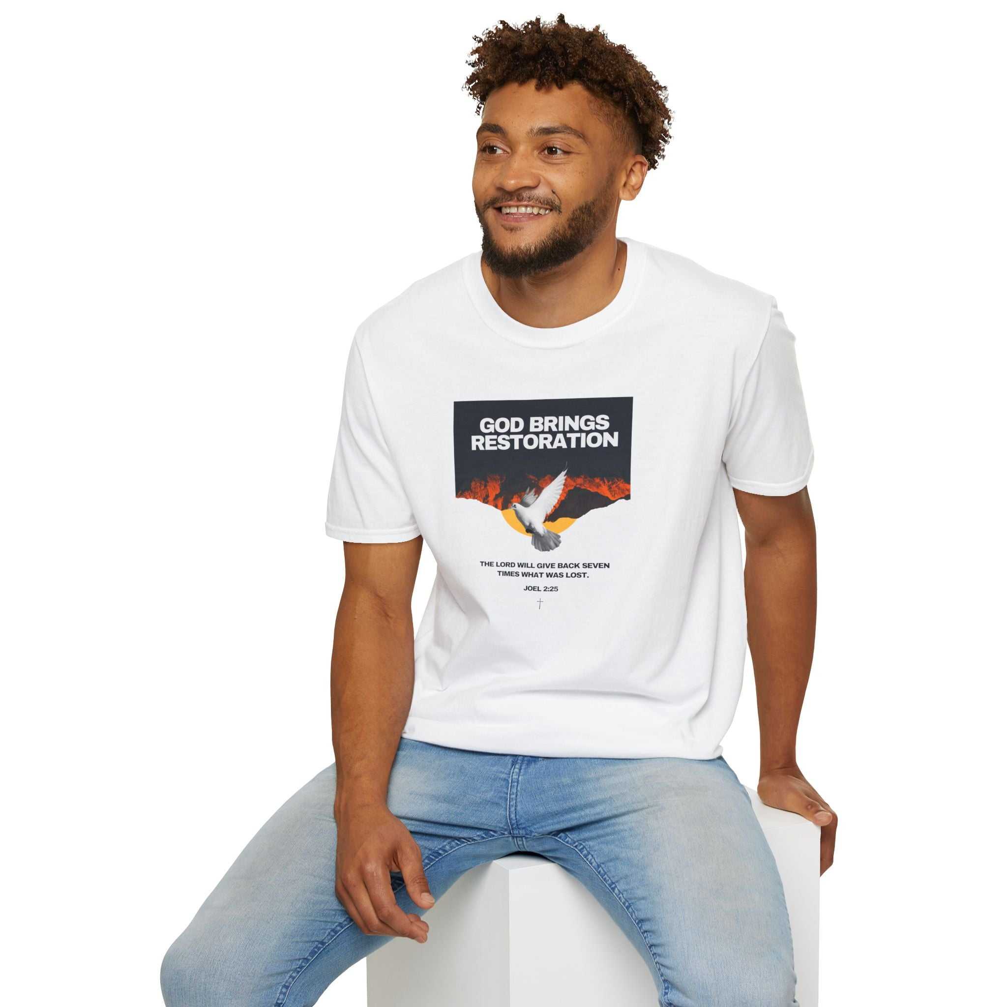 Man wearing white Restored by Grace T-shirt with faith message and jeans sitting on white cube