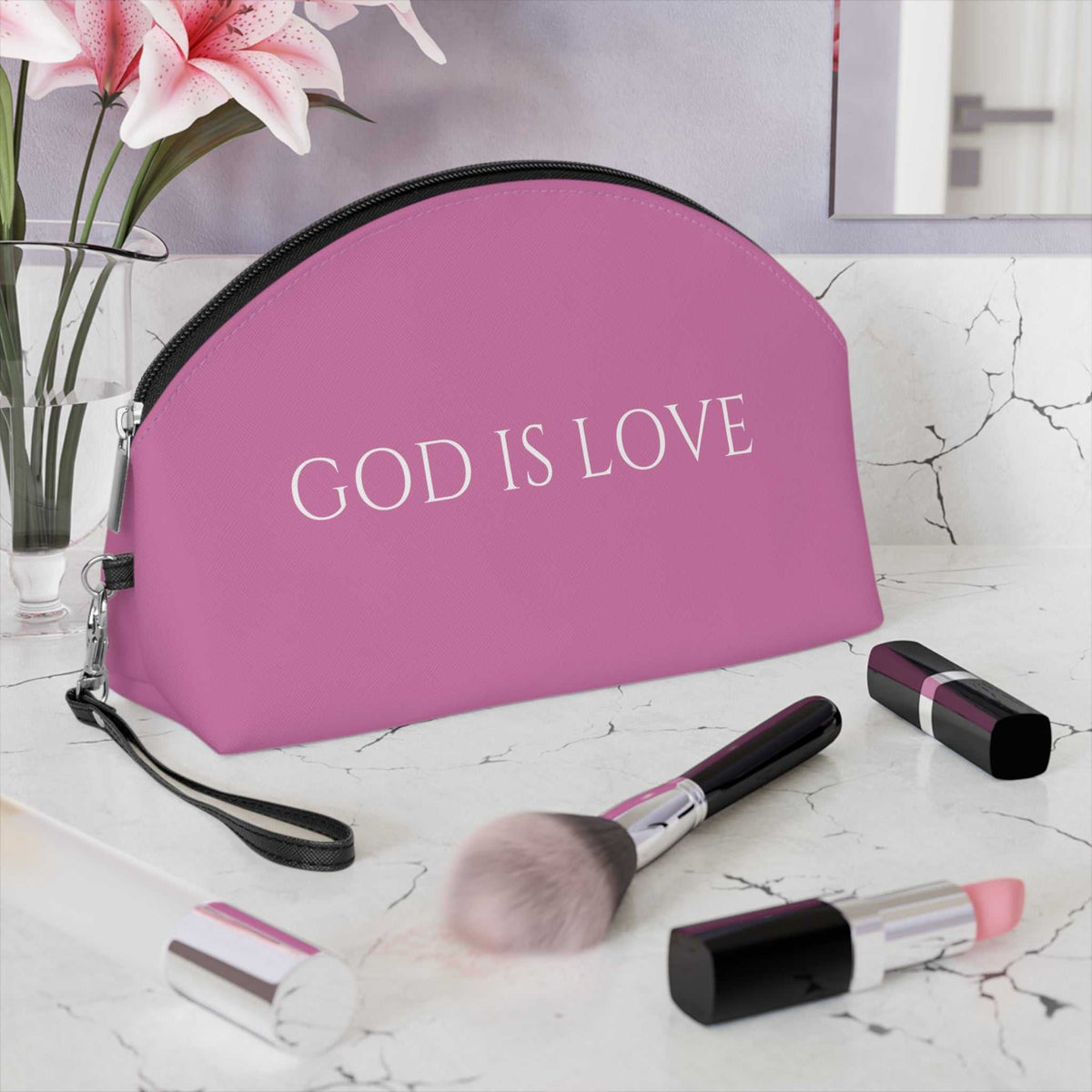 Pink God Is Love makeup bag with detachable strap on marble countertop with makeup brushes and lipstick