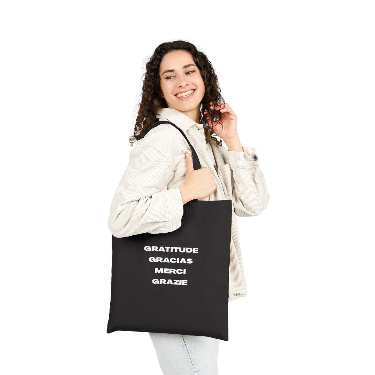 Black cotton canvas tote bag with gratitude text in multiple languages, carried by a smiling woman